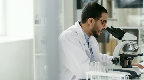 Un Hombre Anotando En Un Papel Su Observación De Una Muestra Bajo Un Microscopio