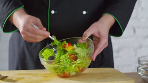 A Chef tossing The Vegetables Salad In A Bowl To Spread The Dressing