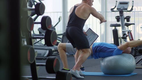 A Gym Instructor Guiding A Man Using The Exercise Balls