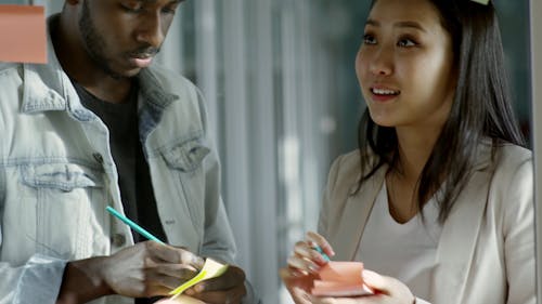 A Man And A Woman Sticking A Note Stick Pad Paper On The Glass Panel