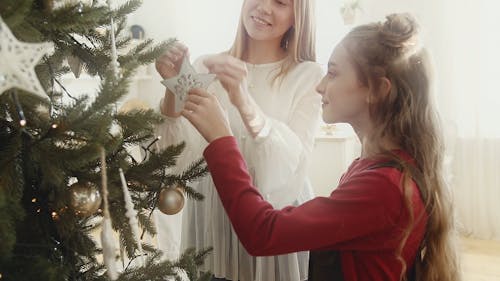 Mother And Daughter Hanging Ornaments Decor On A Christmas tree