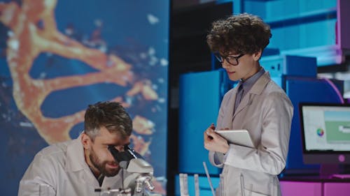 A Woman Taking Note Of A Man's Observation On A Subject Under The Microscope