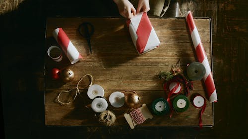 A Person Gift Wrapping A Box Of Present Over A Wooden Table