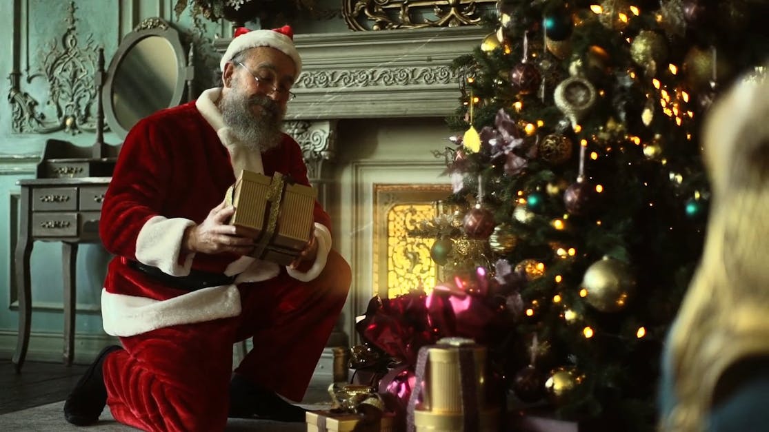 Santa Claus Sneaking To Place A Box Of Gift Under A Christmas Tree Free