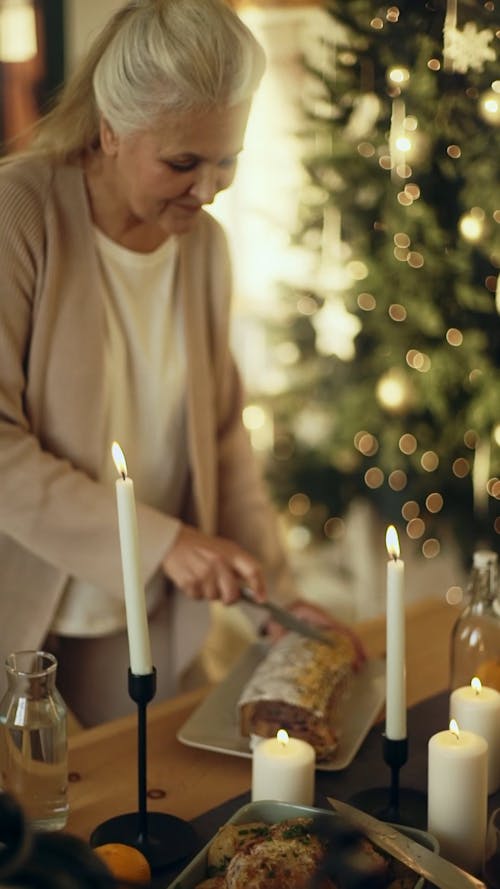 An Elderly Woman Cutting A Cake Using A Knife In The Dining Table