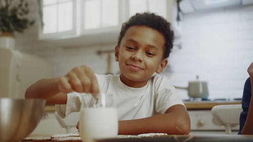 A Boy Dipping A Cookie He Decorated In A Glass Of Milk Before Eating Eat