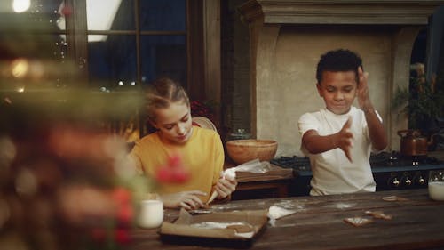 Een Meisje Poedersuiker Decor Op Een Koekje Zetten Terwijl De Jongen Naast Haar Bakpoeder Op Zijn Hand Klapt