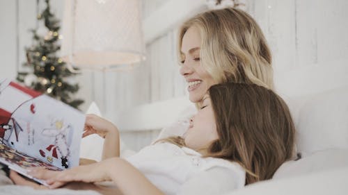 Uma Mãe Abraçando A Filha Na Cama Enquanto Lê Um Livro Infantil