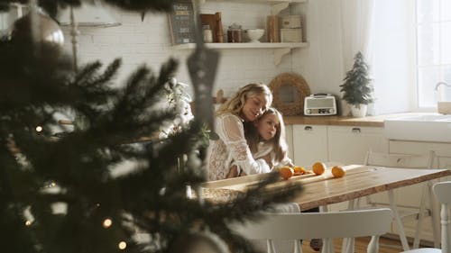 Mother And Daughter Eating Orange Fruit In The Kitchen