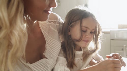 A Girl Peeling An Orange Fruit While Seated On Her Mother's Lap