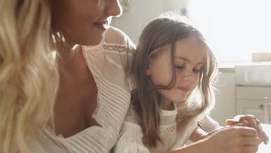 a girl peeling an orange fruit while seated on her mother s lap