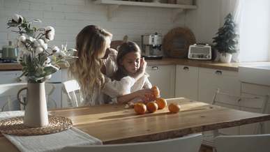 a mother fixes her daughter s hair who is peeling an orange fruit