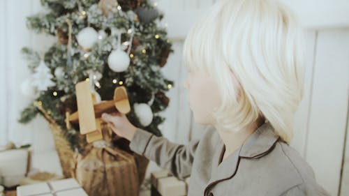 A Boy Playing A Wooden Toy Plane Beside The Christmas Tree