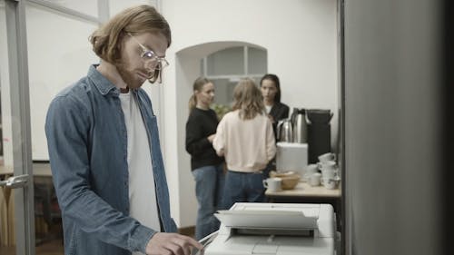Man Working Using A Copying Machine While His Colleagues Are Having Their Break Time
