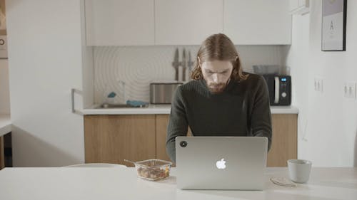 A Man Having His Breakfast While Working On A Laptop In The Pantry