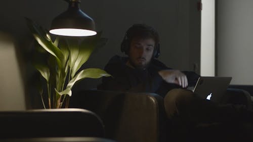 Um Homem Toma Uma Bebida Enquanto Trabalha Em Um Laptop Com Fones De Ouvido