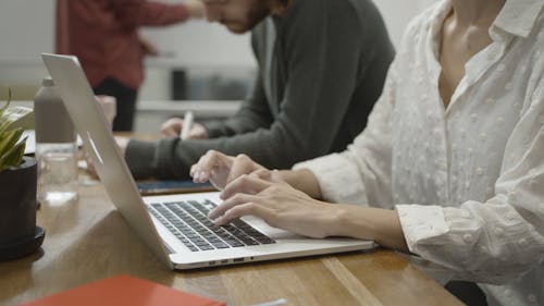 Женщине, работающей за ноутбуком, помогает коллега, сидящий рядом с ней