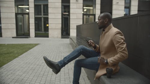 Uomo Seduto Al Di Fuori Di Un Edificio Guardando Il Suo Telefono Durante L'attesa