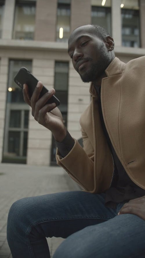 Man Sitting Outside A Building While Looking At His Phone