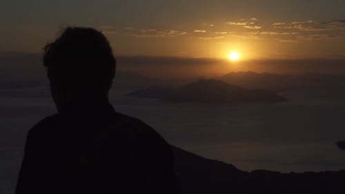 一个人在山顶上看着地平线上的日落美景