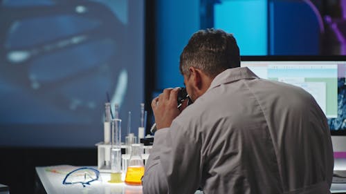 A Man On A Microscope Studying A Sample And Recording It In A Computer