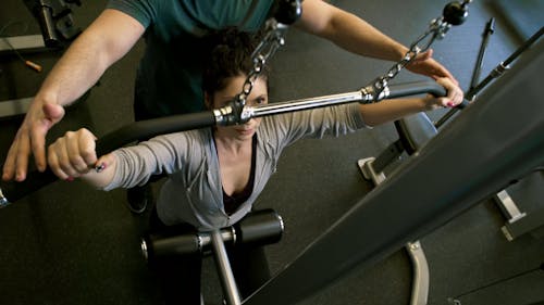 Een Man Een Vrouw Helpen Bij Het Gebruik Van De Apparatuur Voor Platte Pulldown Gewichten In Een Sportschool