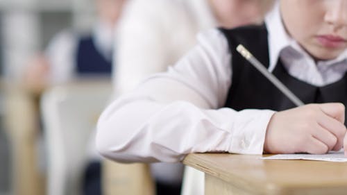 A Child Using A Pencil Writing On A Paper Inside A Classroom