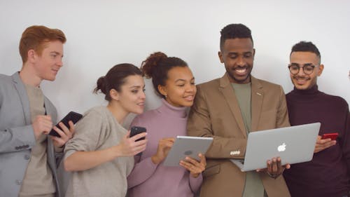 A Group Of People Standing In Front Of A White Wall Busy With Their Electronic Gadgets