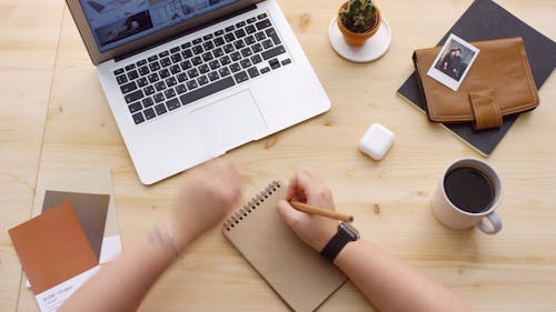 A Person Writing In A Notepad About A Photo Stored In A Laptop