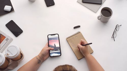 Person Looking At Pictures In His Phone While Making Notes