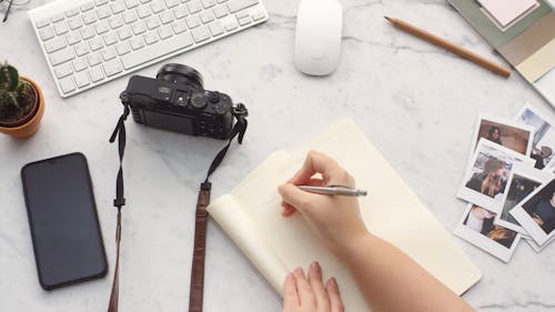 A Woman Writing On A Notebook Over A Table