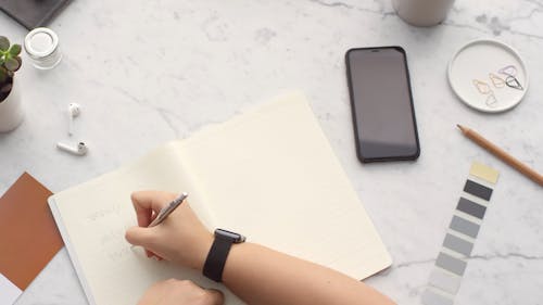 A Person Writing On A Notebook Using a Pen