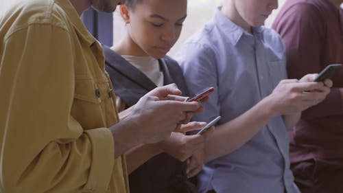 A Group Of People Standing Side By Side With One Another Are Busy Using Their Cellular Phones