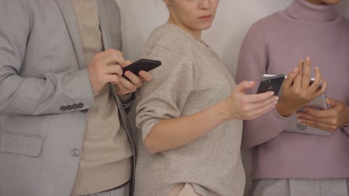 A Group Of People Standing Next To Each Other Are Busy Using Electronic Gadgets