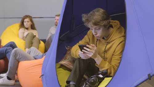 一个年轻人坐在摇摆的帐篷上时使用他的手机