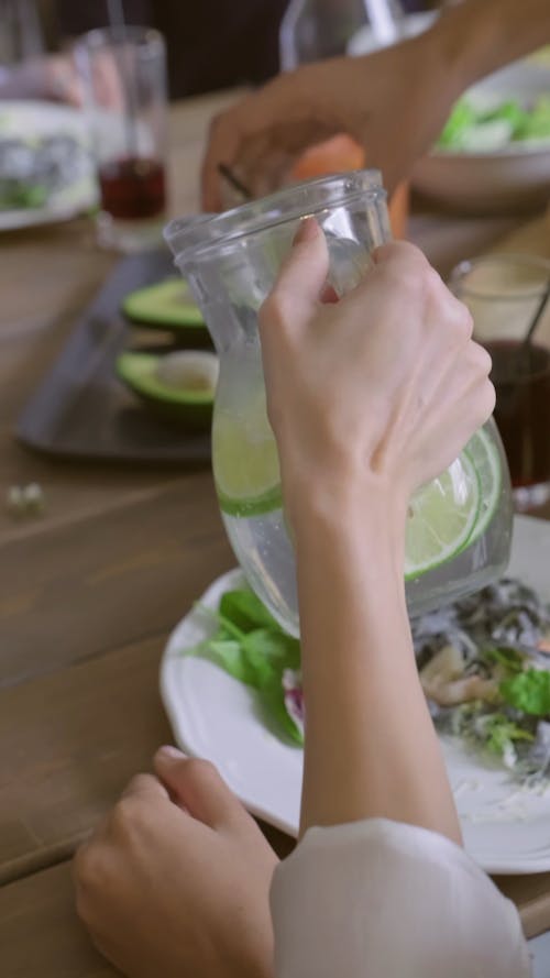 A Woman Pouring Lemonade On Glasses Of People She Is Eating With