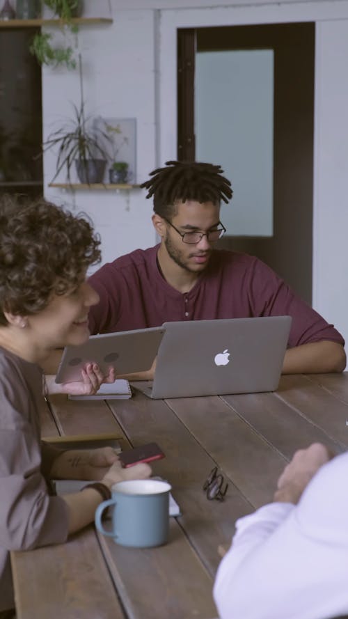 A Group Of People Busy Working While Gathered Around A Wooden Table