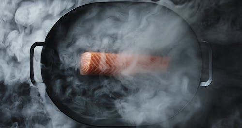 A Blow Of Smoke For Effect On A Slab Of Salmon Meat On A Sizzling Tray