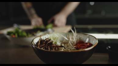 a person uses a whit cabbage vegetable for added toppings in a noodle soup bowl dish