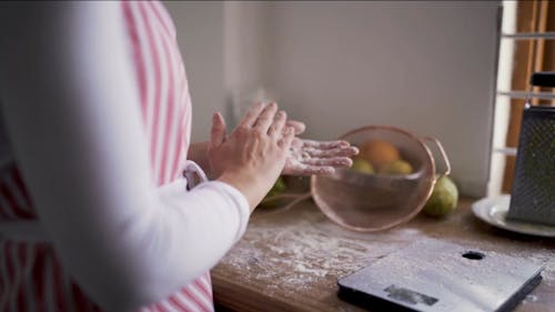 Женщина вытирает излишки муки с рук во время выпечки