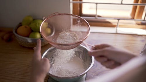A Person Straining The Flour To Be Used In Baking
