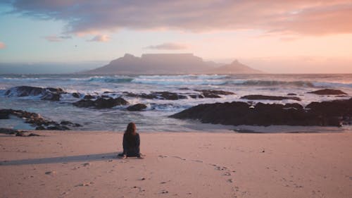 A Woman Seated On The Beach Sand Enjoying The Table Mountain View