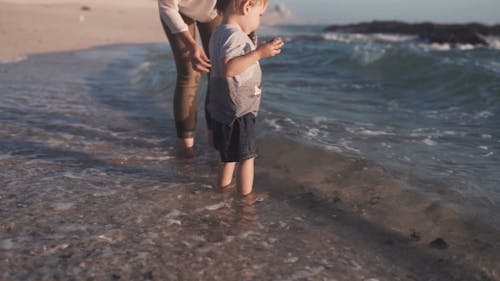 A Mother And Child Standing In The Beach Water Throwing Rocks