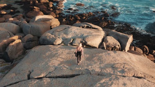 A Woman Laying Her Yoga Mat Over A Boulder Of Rock By The Sea Coast