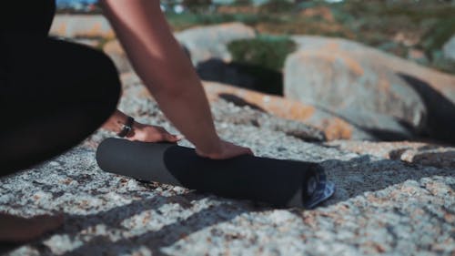 A Woman Rolling Out A Yoga Mat Over A Flat Rock Formation Surface