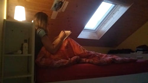 ペンでノートに書いているベッドの女性
