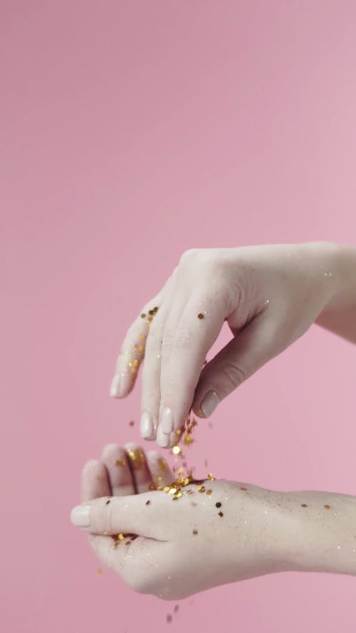 A Person's Hands Playing With Gold Confetti