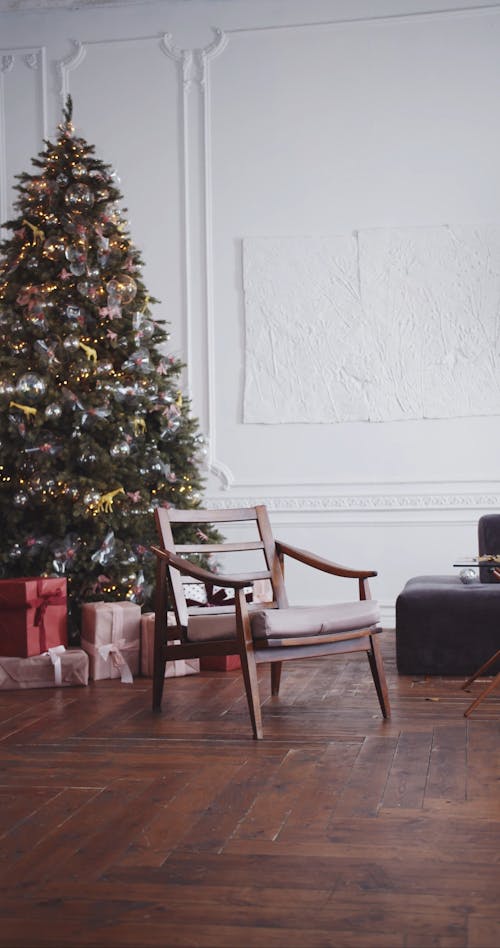 Eine Frau, Die Ein Silbernes Kleid Trägt, Sitzt Auf Einem Stuhl Vor Einem Weihnachtsbaum Und Schlägt Eine Pose