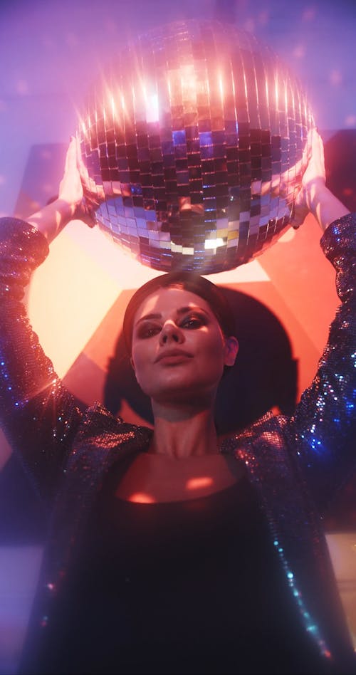 A Woman Holding A Mirror Ball Above Head To Reflect A Spot Light Into Dots Of Small Lights