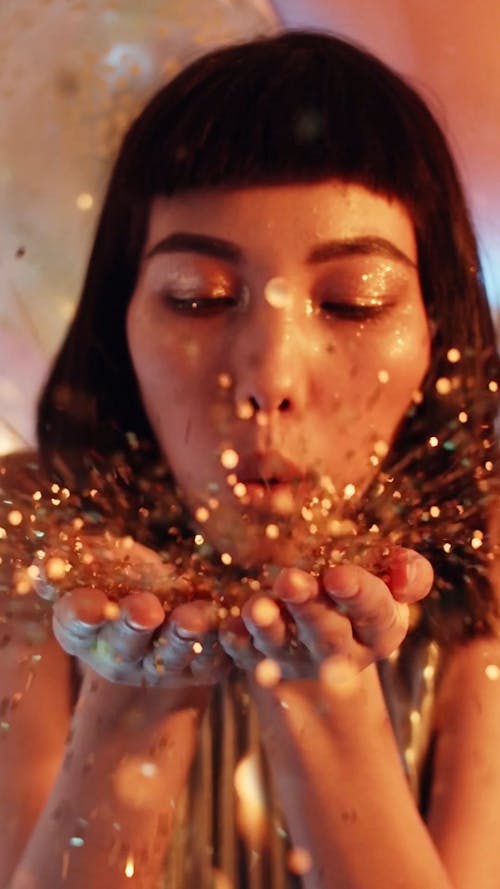 A Woman Blowing Off Gold Confetti From Her Palms On A Repetitive Video Footage